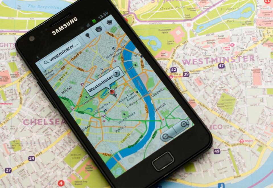 A samsung tablet sits on top of a map of London. The tablet screen shows a digital map with a pin marking Westminster.