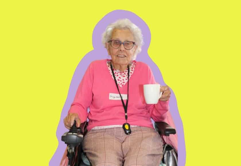 An older white woman with short white hair and glasses using a mobility chair and holding a white mug smiling at the camera. The background is a coloured graphic.