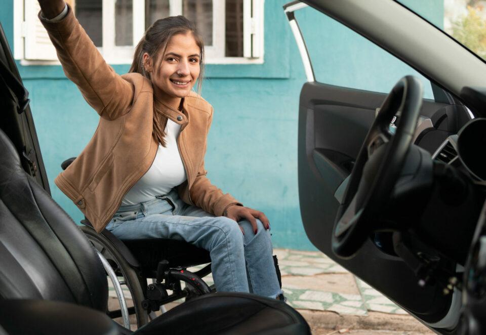 A woman using a wheelchair is smiling at the camera through the open door of a car.
