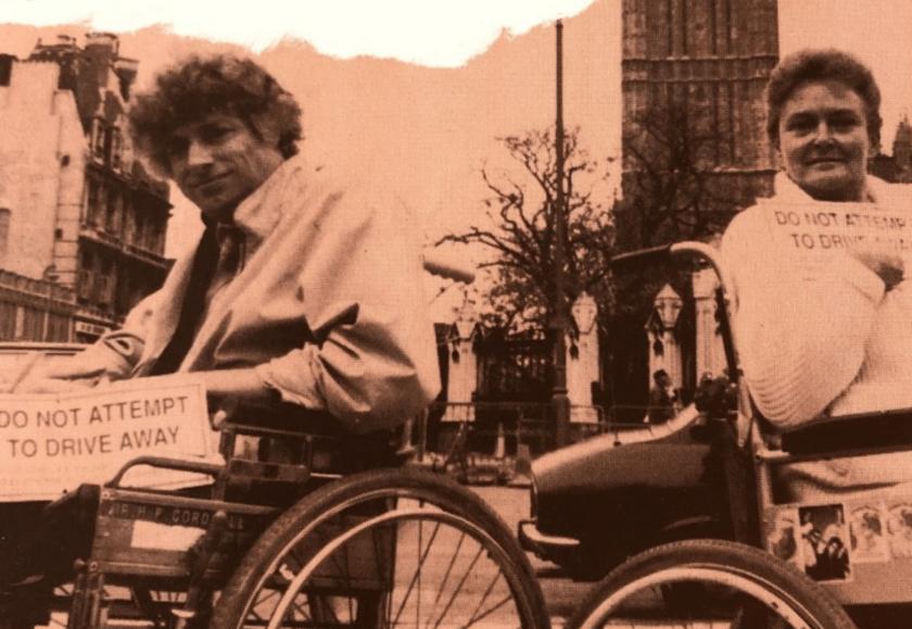 Photograph of two wheelchair users holding signs that read 