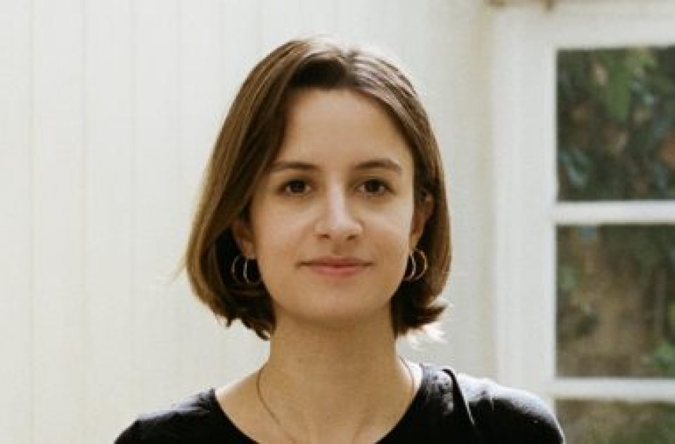 Celestine, a white woman in her late twenties, looks at the camera with a slight smile. She wears a black t-shirt and her brown hair is worn in a bob.